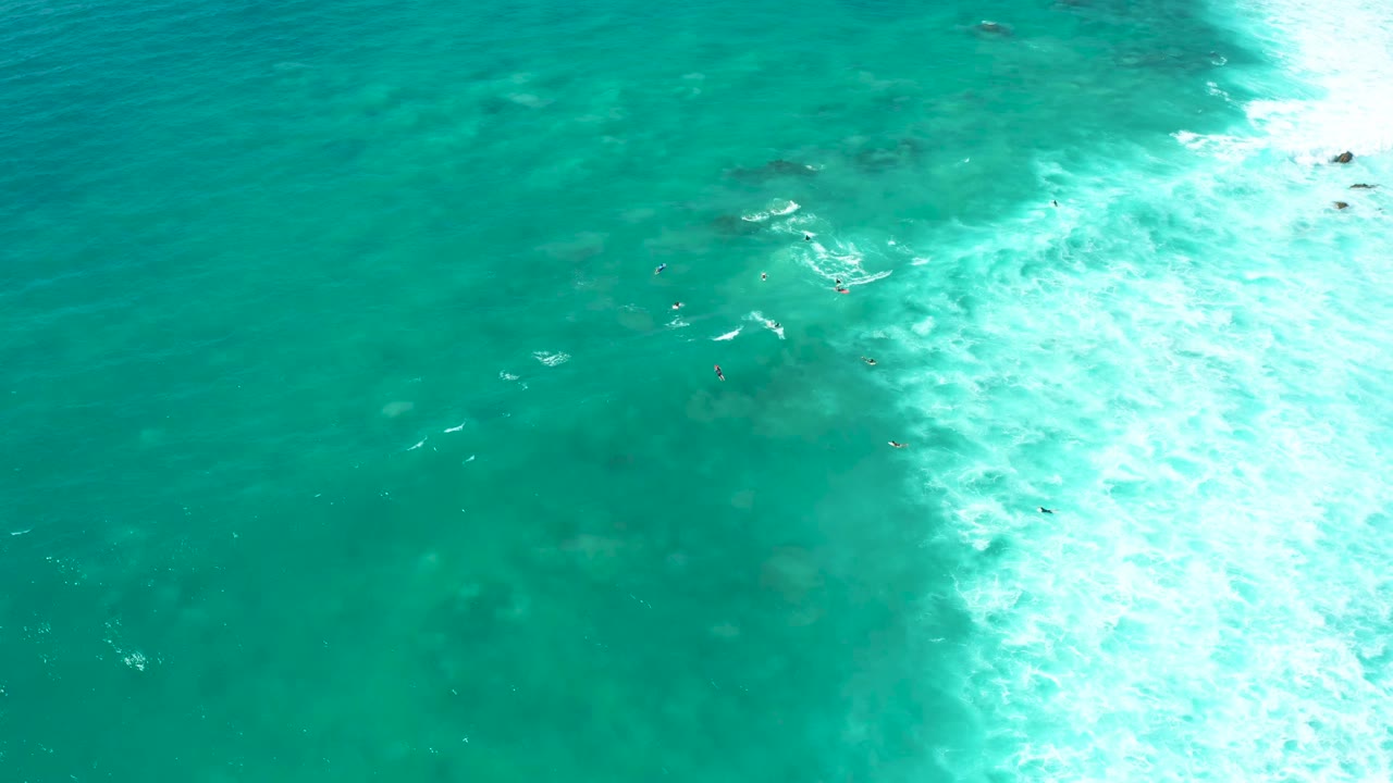 Turquoise shallow water with swimmers near a bright band of foam.
