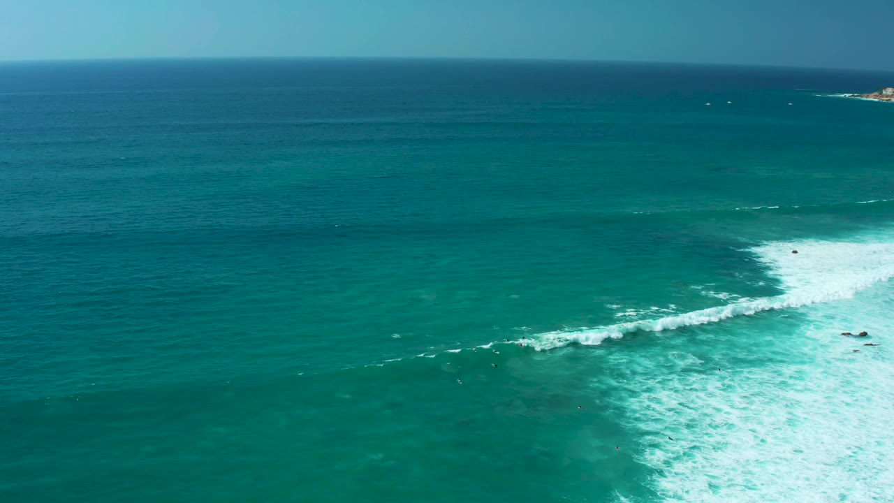 Aerial view over Marquis Los Cabos ocean water with the breaking wave shifted toward the right edge and a broad calm surface to the left, with no visible people.