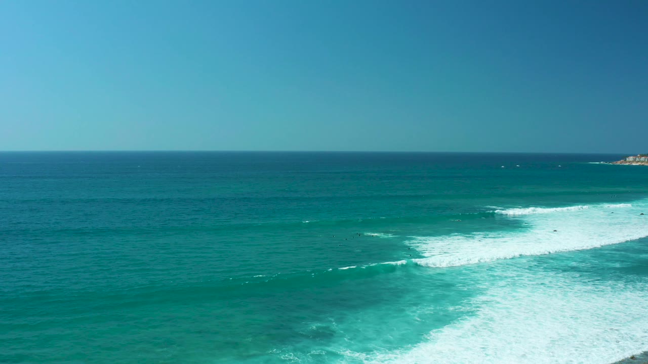 Aerial view of turquoise ocean waves breaking into white foam under a clear sky.