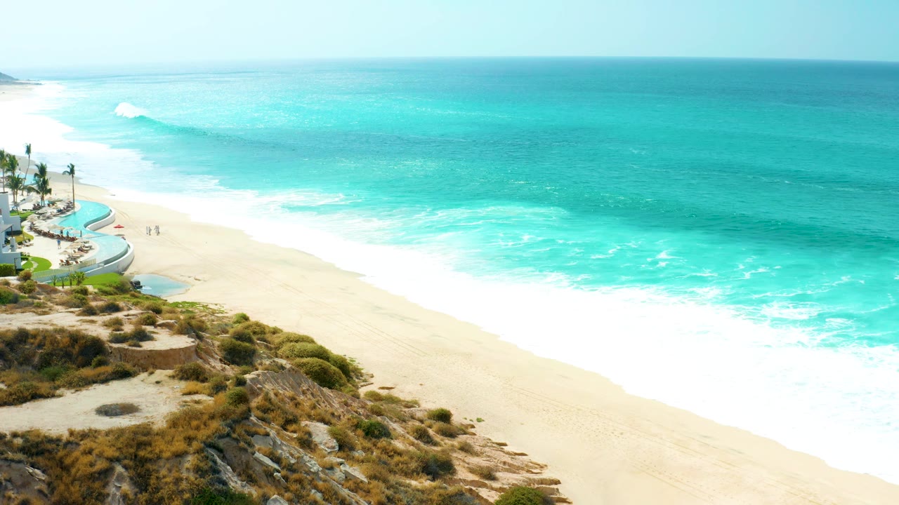 White surf rolls onto a sandy beach under a hazy blue ocean horizon.