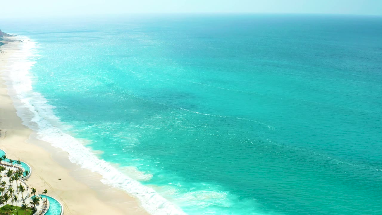 The fourth frame keeps the surf band close to the left side, showing turquoise water, pale beach, and a small corner of resort landscaping at Marquis Los Cabos, with no visible people.