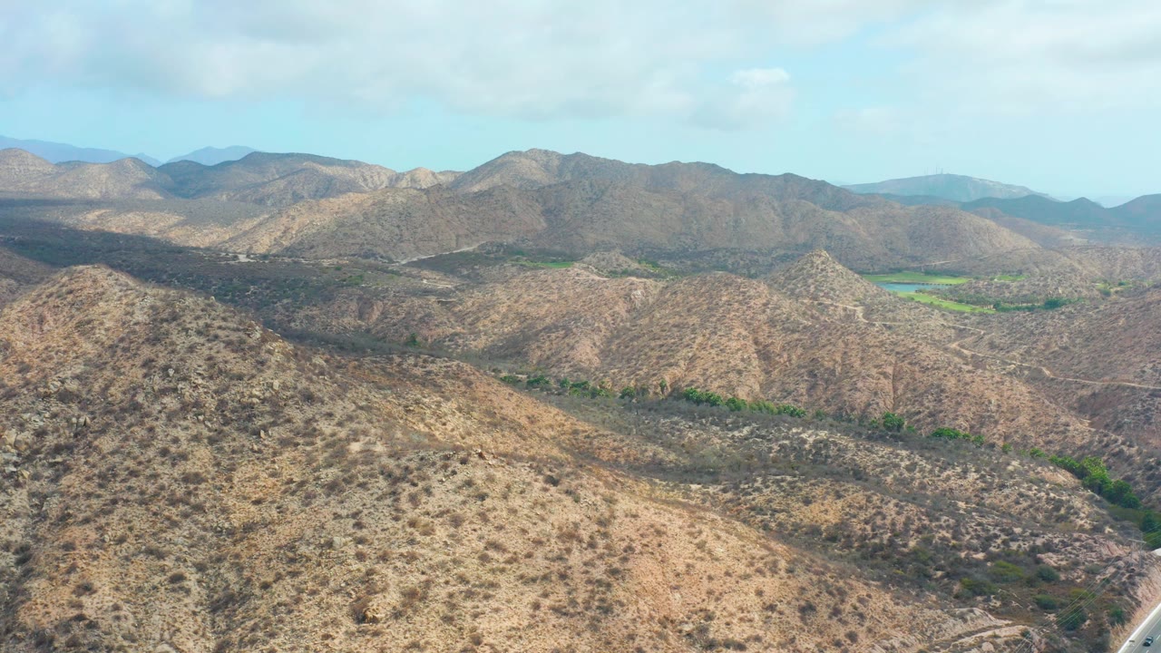 Aerial view of dry mountain ridges and valleys under a pale blue sky.