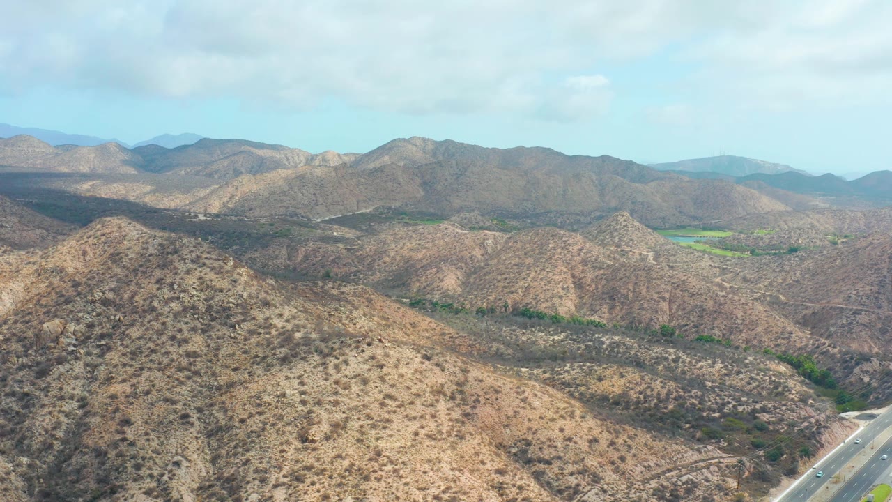 Mountain valley with dry hills, clouds, and a highway along the lower edge.