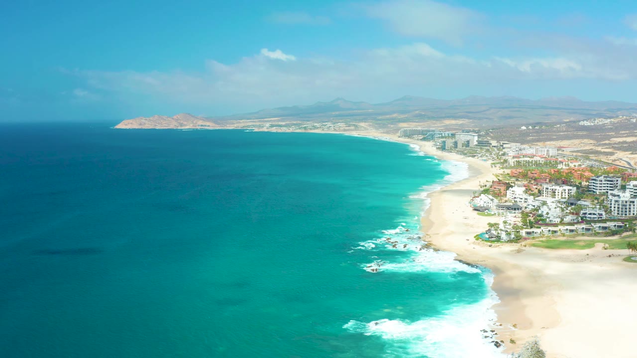 Aerial beach view with waves breaking near shoreline buildings.