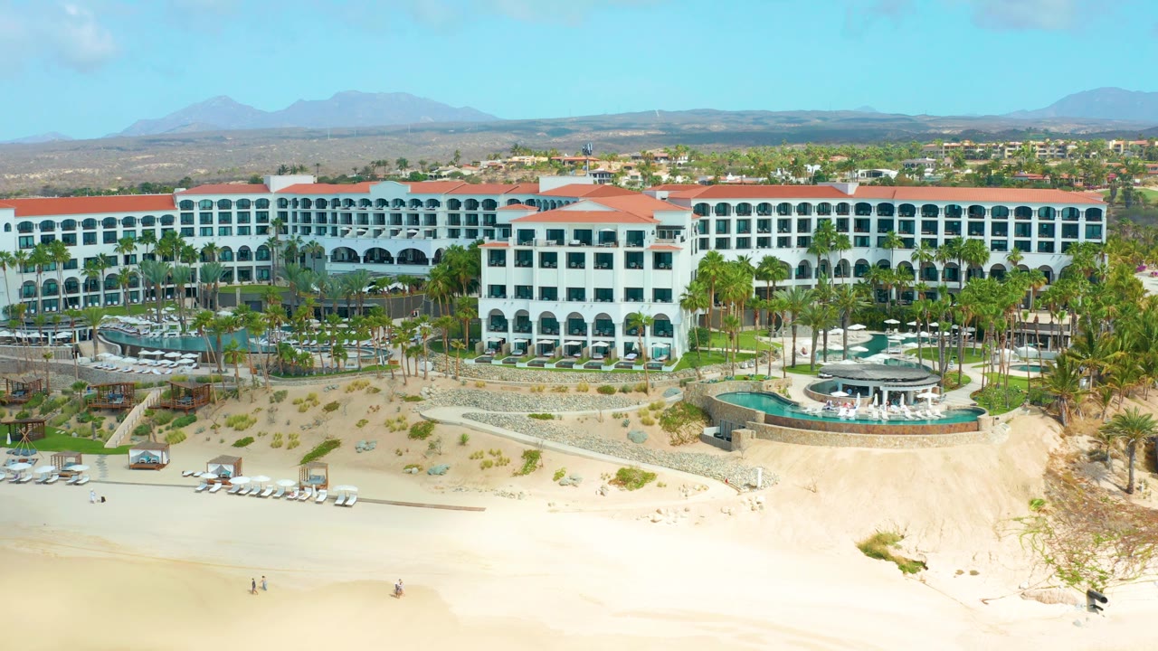 White resort buildings and pool area above a broad sandy beach.