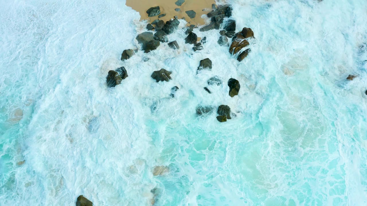 Overhead surf and dark rocks near a sandy shoreline.