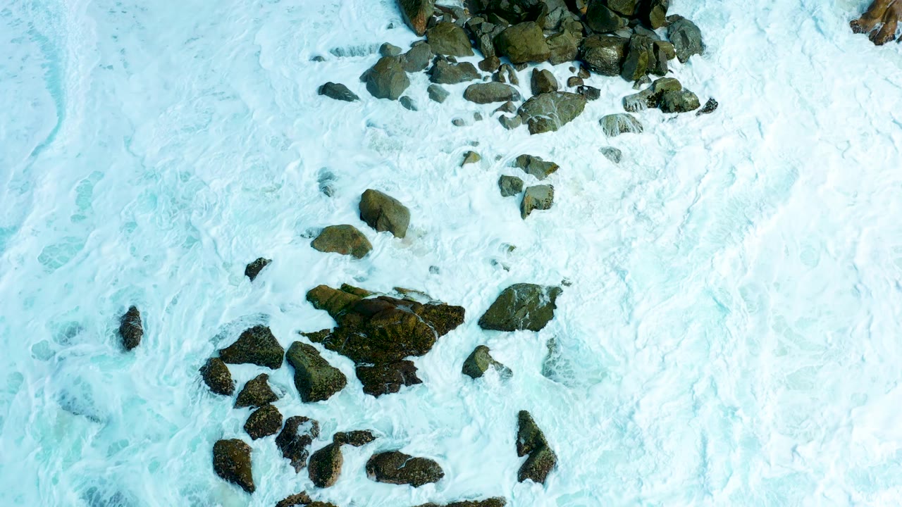 Overhead surf foam around dark shoreline rocks