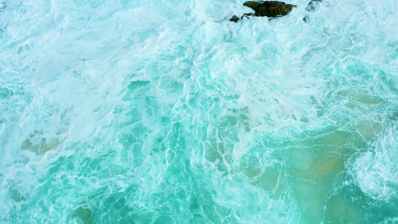 Overhead turquoise surf with white foam and a dark rock near the top edge.