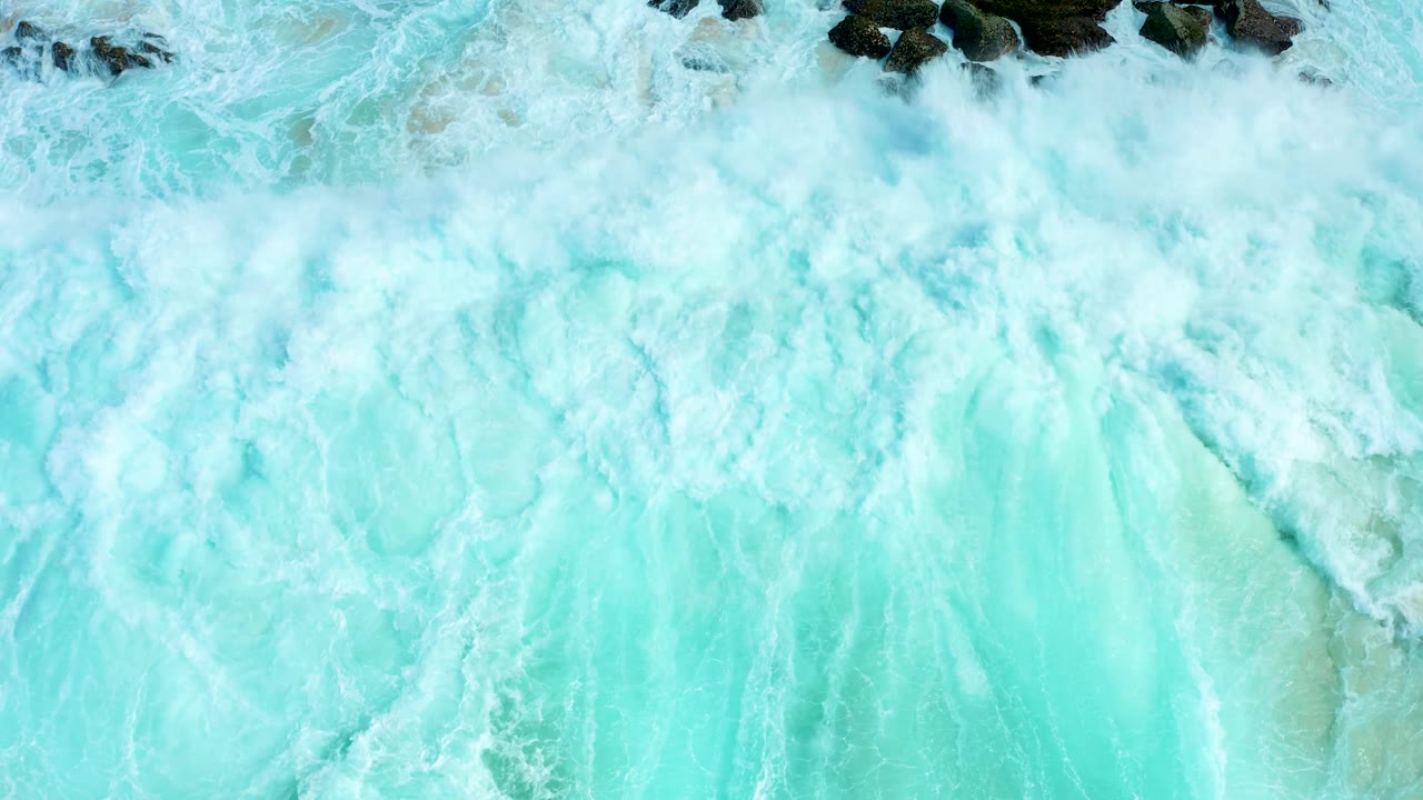 Churning white foam fills most of the overhead frame at Marquis Los Cabos, Mexico, with a few dark rocks still visible along the upper edge and no visible people.