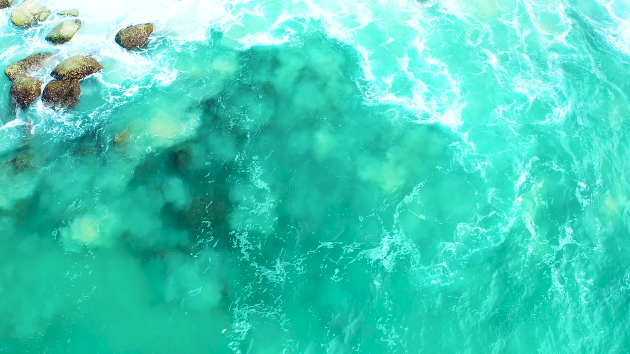 Aerial turquoise surf with rocks near the top edge