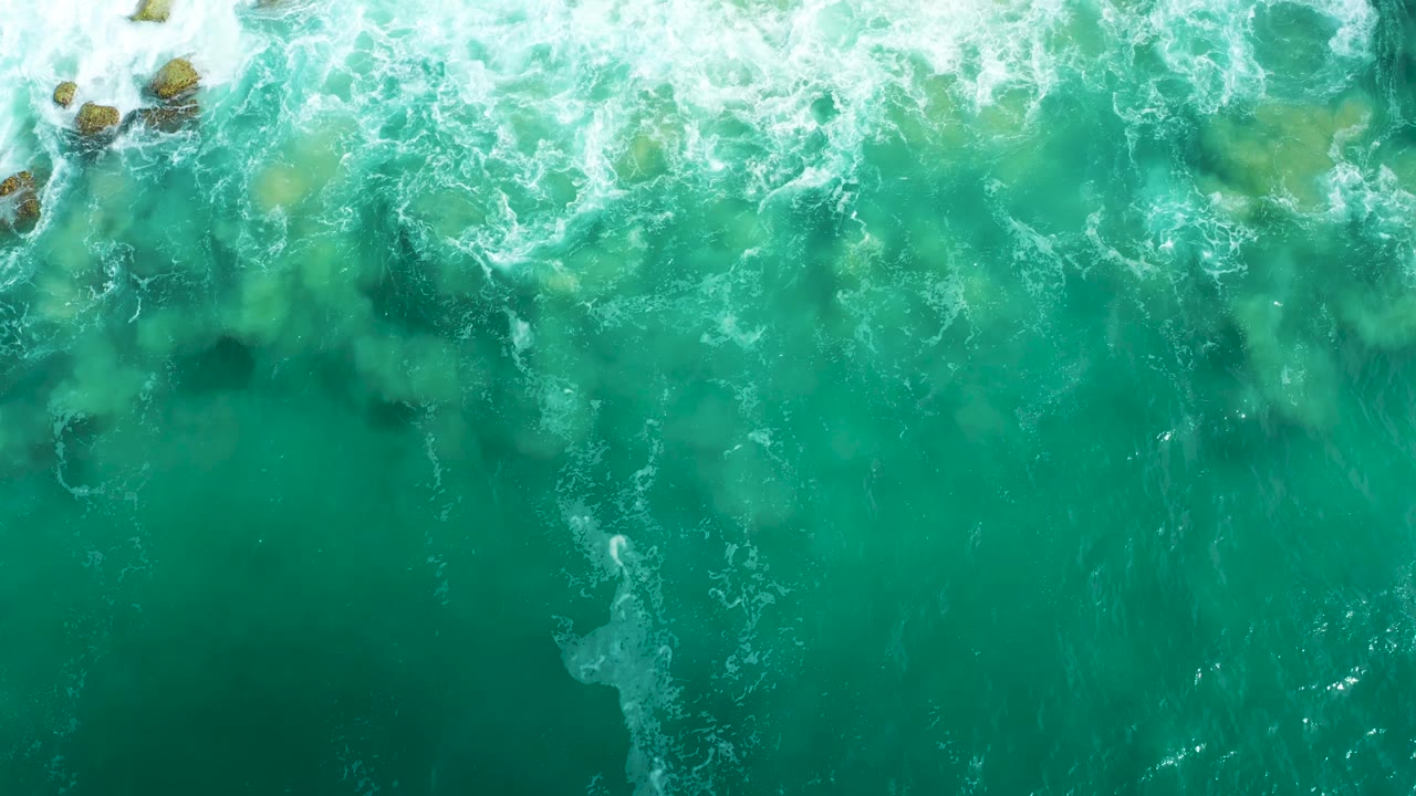 Clear turquoise water reveals pale rocks beneath thinning foam.