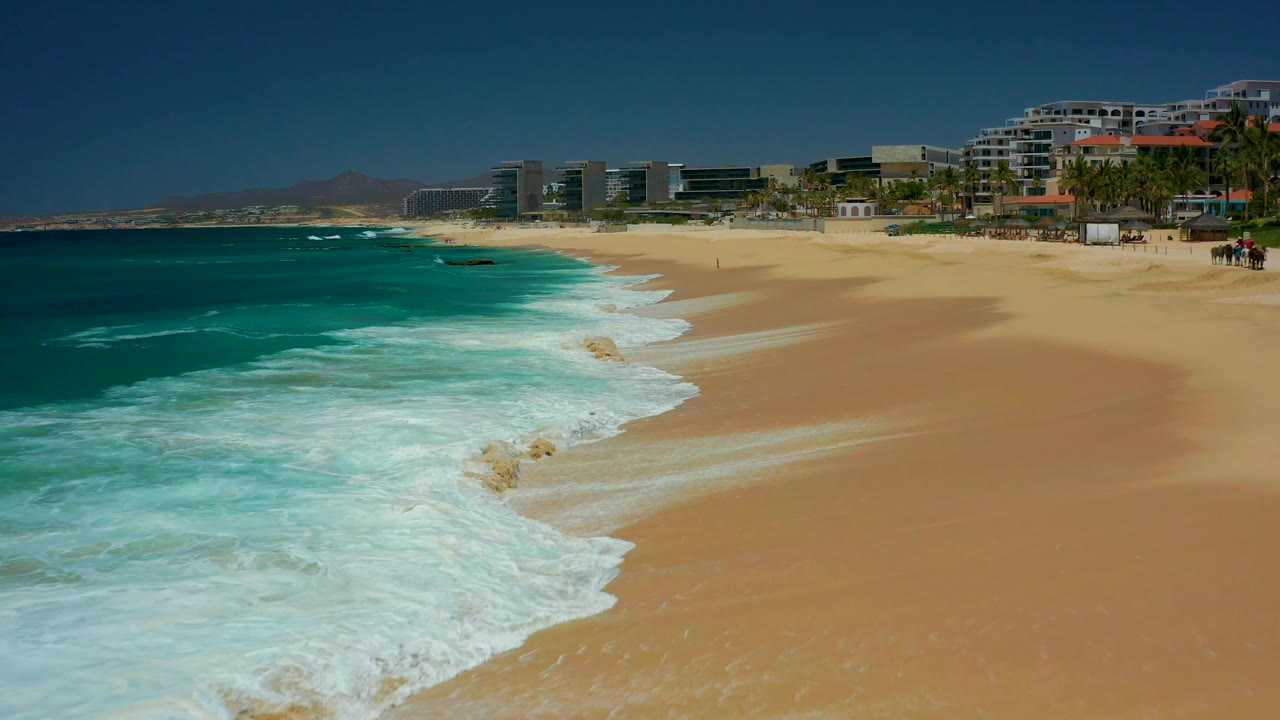 Foamy wave line curving across sand with beachfront buildings behind it.