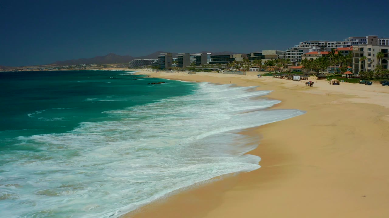Turquoise waves washing onto a sandy beach beside resort buildings.