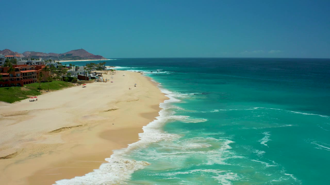 Foamy surf spreads farther across the sandy shoreline beside blue ocean water.