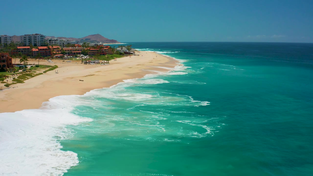 White waves roll across turquoise water toward a sandy resort beach.