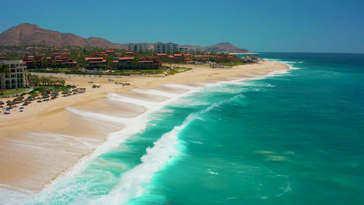 Wide aerial beach view with waves breaking diagonally along the shore.