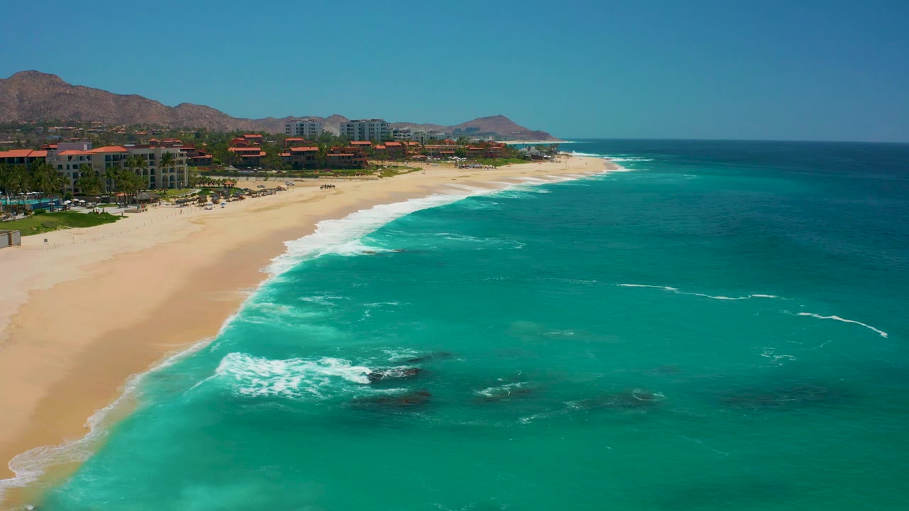 Aerial view of turquoise surf breaking along a sandy resort beach