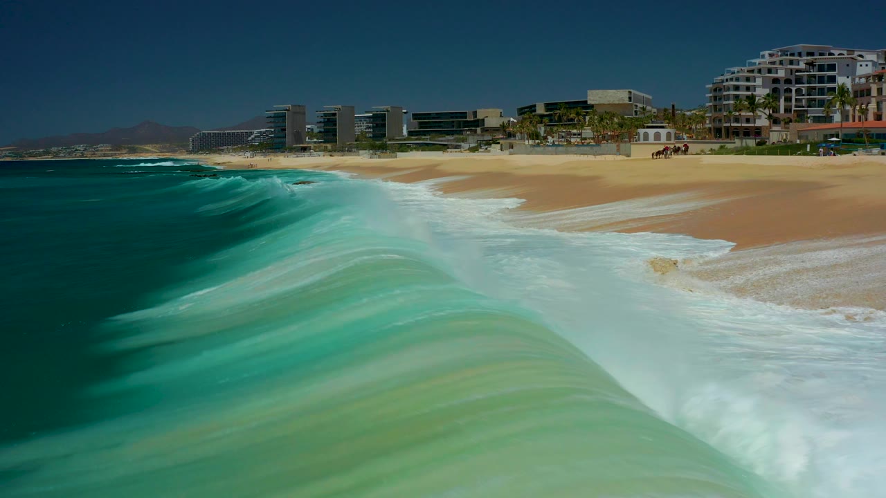 Breaking wave spreading whitewater onto tan sand