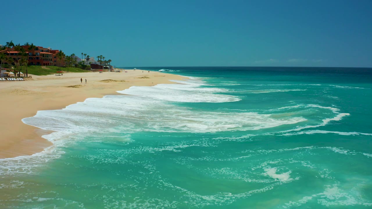 Wide beach and turquoise surf with resort buildings in the distance.