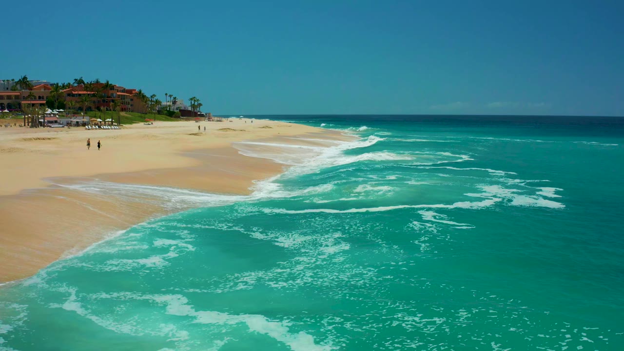 White foam spreads across shallow turquoise water beside a pale sand beach.