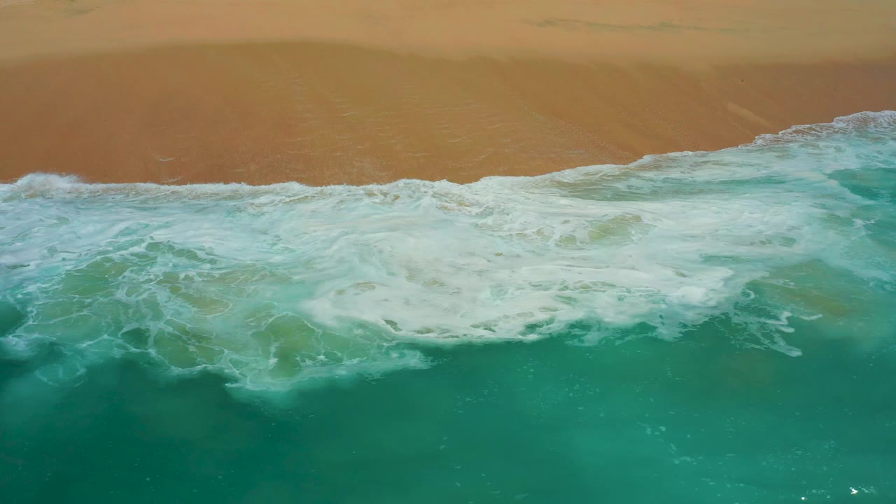 Overhead beach frame at Dreams Los Cabos where the foamy wave edge pushes farther toward the upper sand band, no visible people.