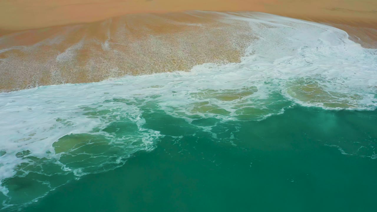 Overhead surf washing across tan sand and green water