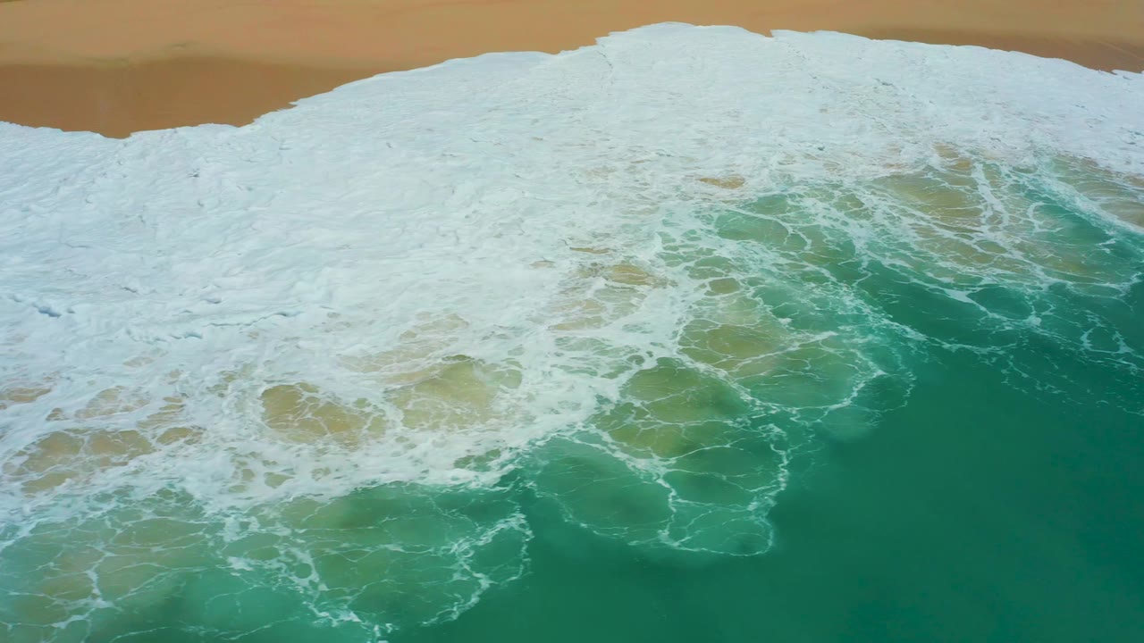 Breaking wave foam spreading over shallow turquoise water.