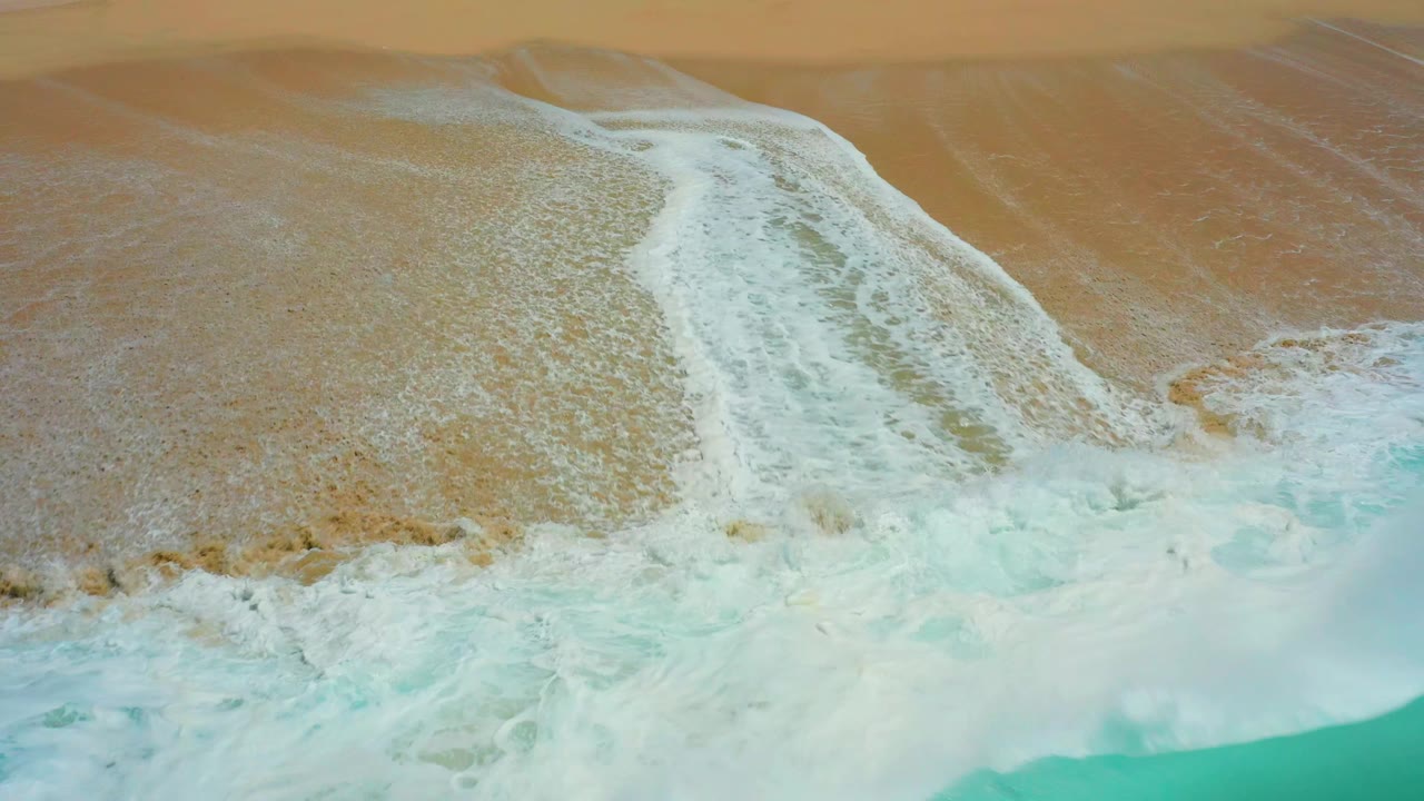White foam receding across wet sand beside turquoise water