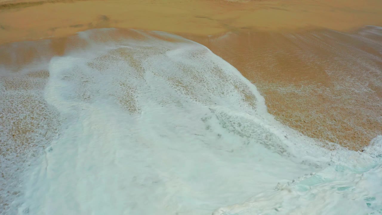 Wave foam beginning to recede from the sandy shore.