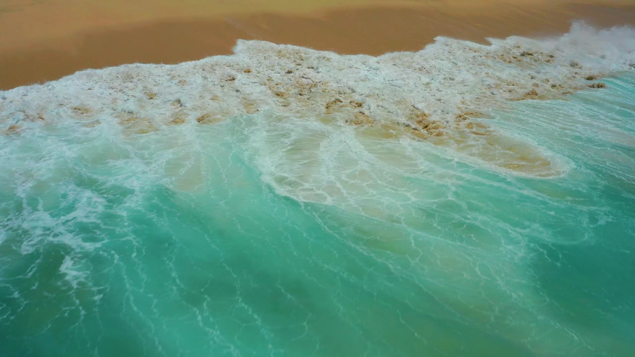 Top-down surf breaking on tan sand