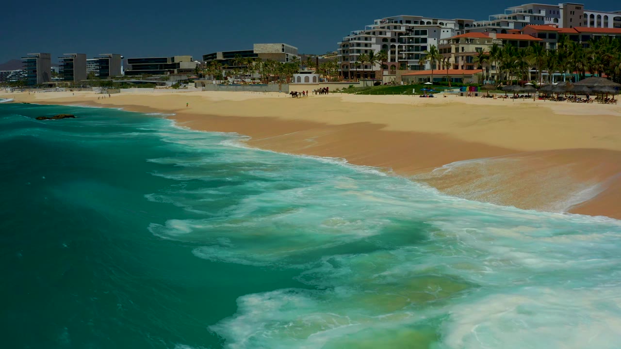 White surf spreads closer to shore below beachfront buildings.