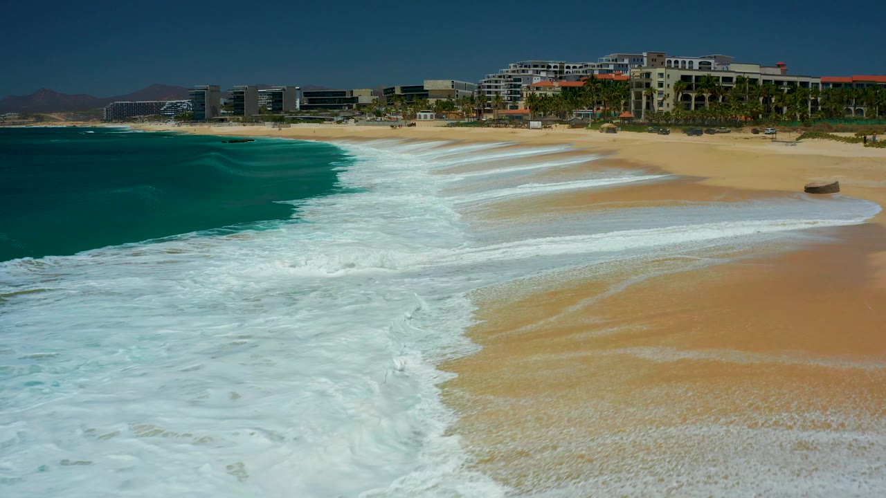 Wave foam pulls along the shoreline with resort buildings in the background.