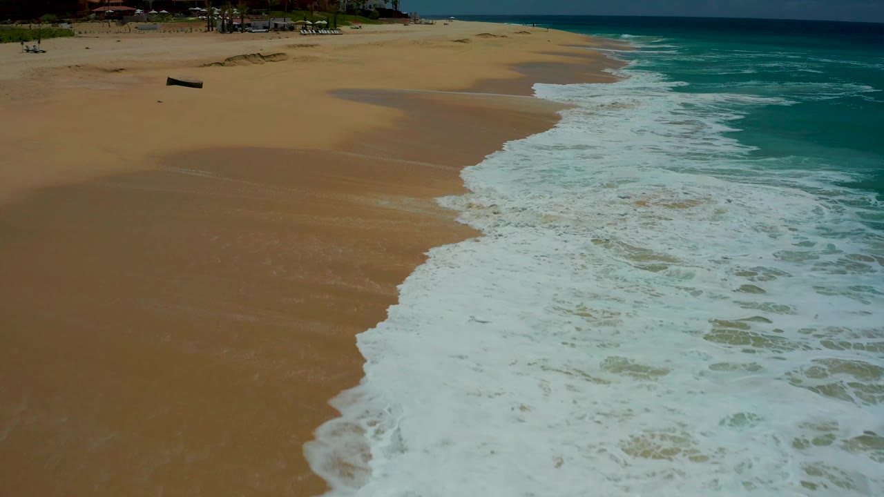 At the Mexico beach location, a thicker sheet of white surf fills the lower right while smooth tan sand remains open on the left, with no visible people.