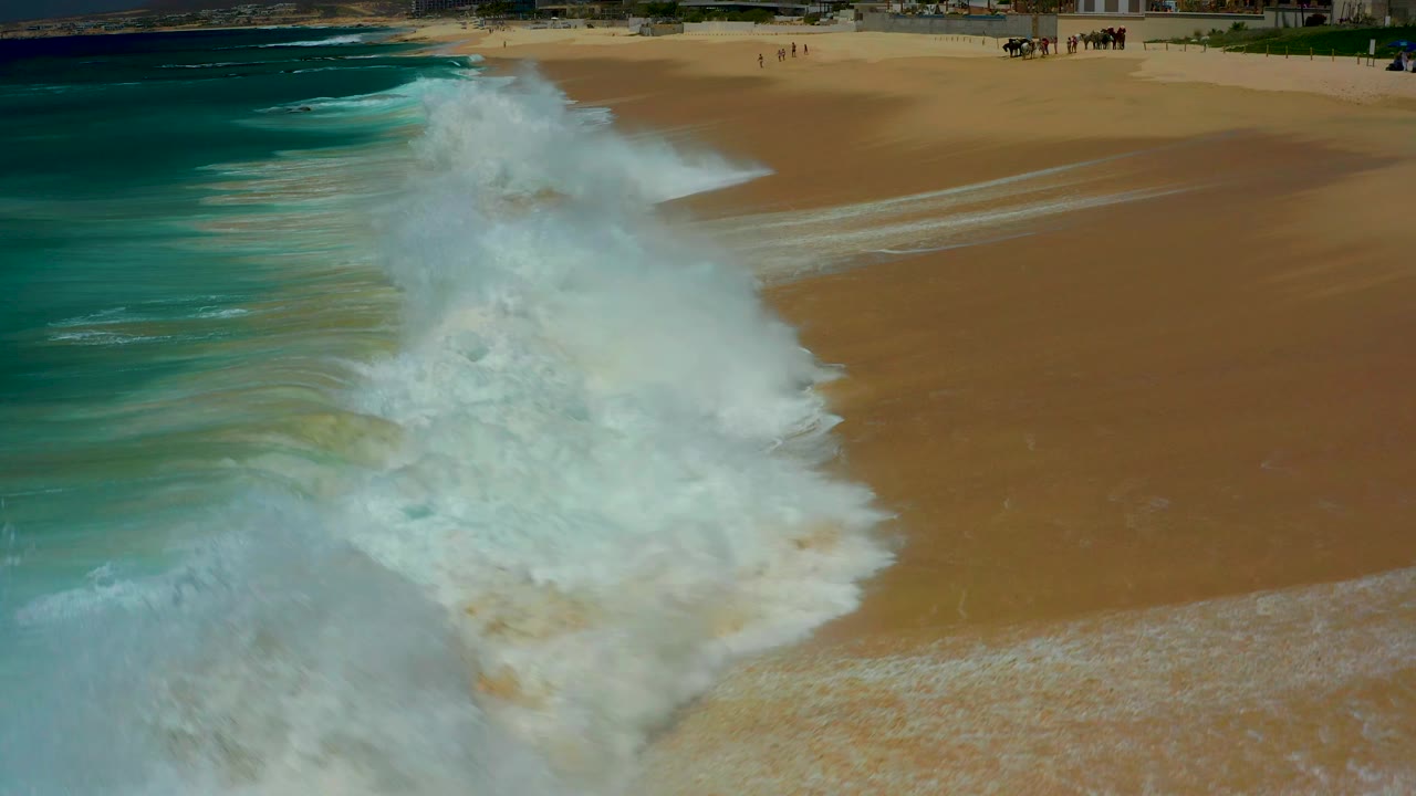 White surf spreads farther across the sandy shoreline.