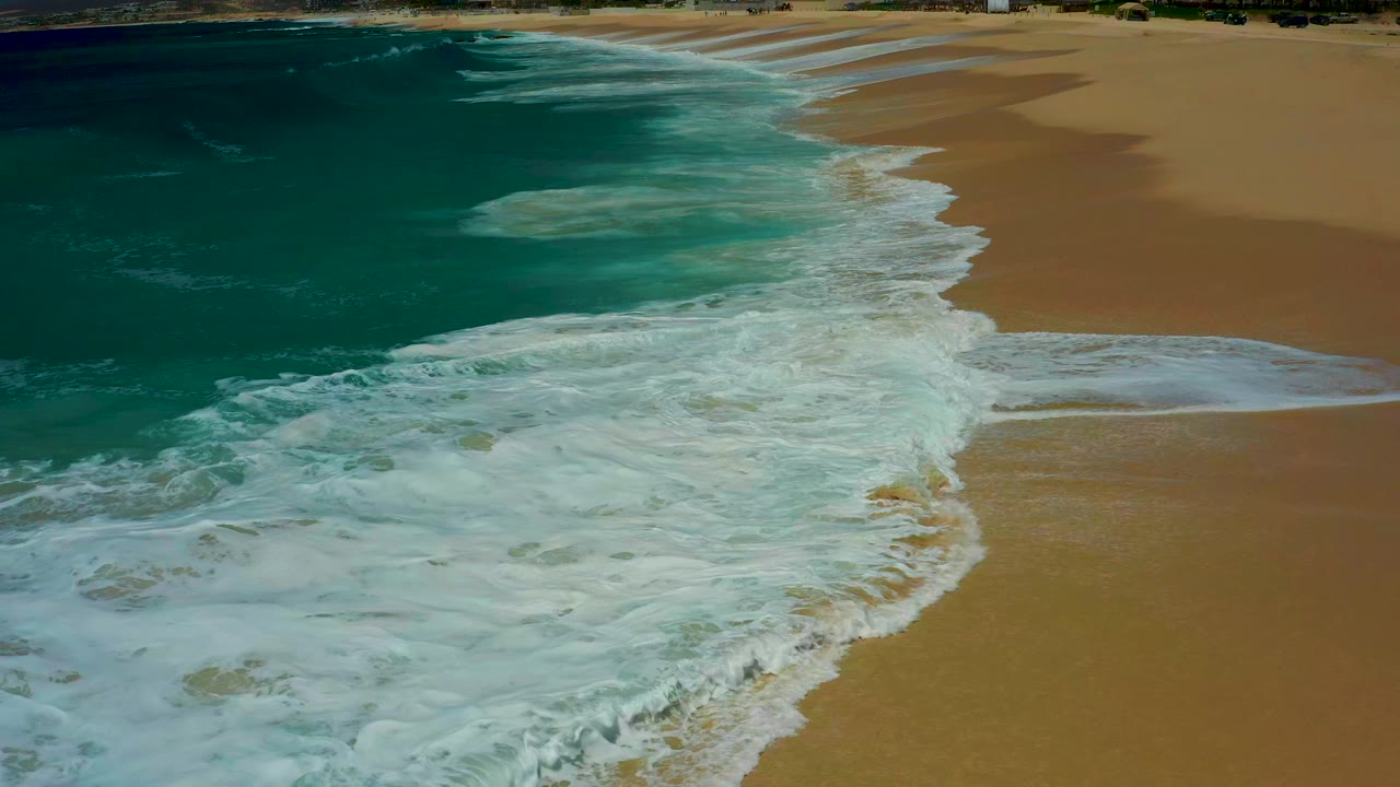 Ocean foam advances farther over wet sand beside turquoise water.