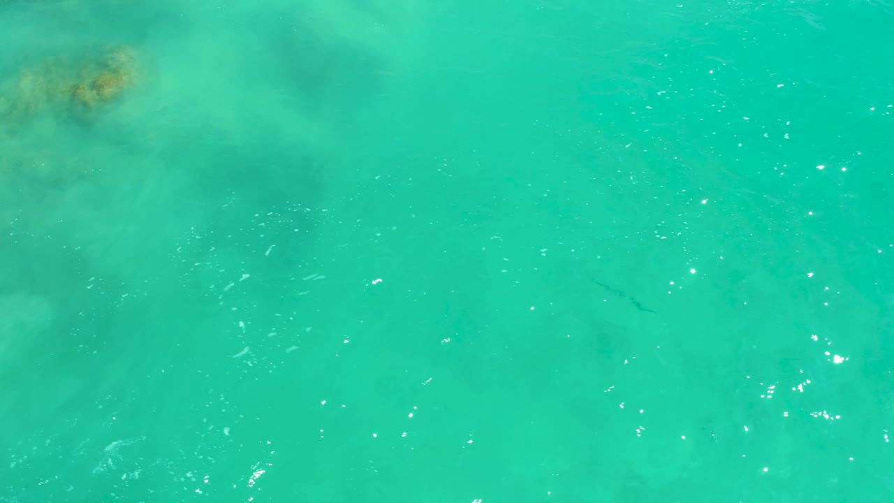 Aerial frame of clear turquoise water at Dreams Los Cabos, showing small dark fish shapes under gentle ripples and no visible people.
