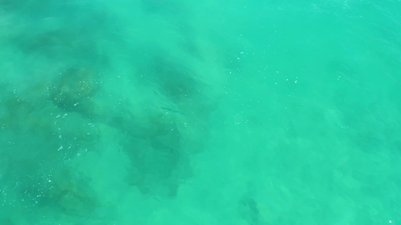 Clear turquoise water at Dreams Los Cabos shows darker underwater rock shapes beneath the surface, tiny bubbles, and no visible people.