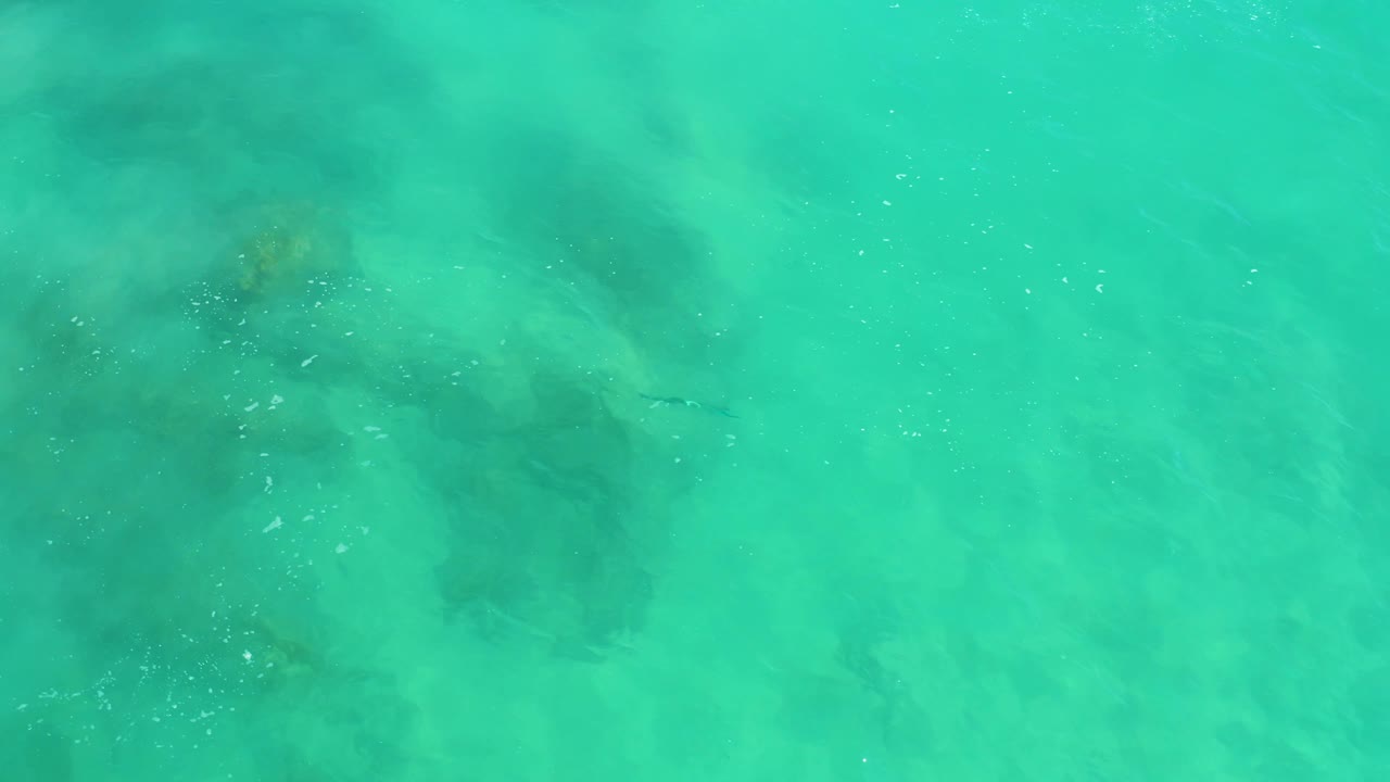A softer section of turquoise water at Dreams Los Cabos shows muted underwater rocks, faint fish shapes, surface haze, and no visible people.