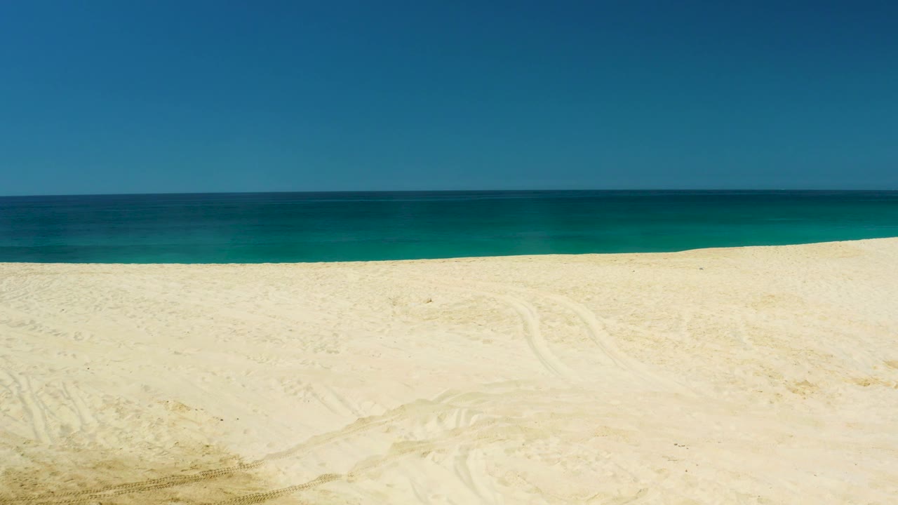 At 0:01, the frame shows more pale beach than surf at Dreams Los Cabos, with the ocean running level across the middle and no visible people.