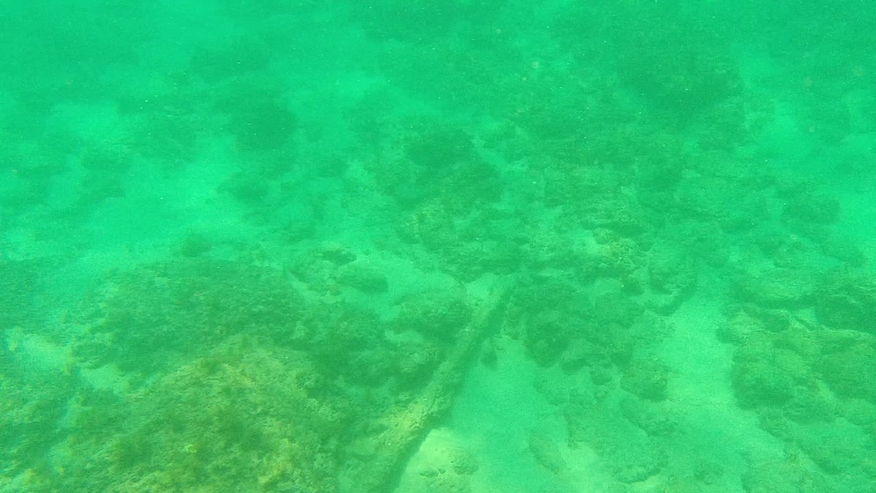 Underwater view in Palmilla Los Cabos with larger rock clusters crossing the center of the frame and sandy bottom visible between them, with no visible people.