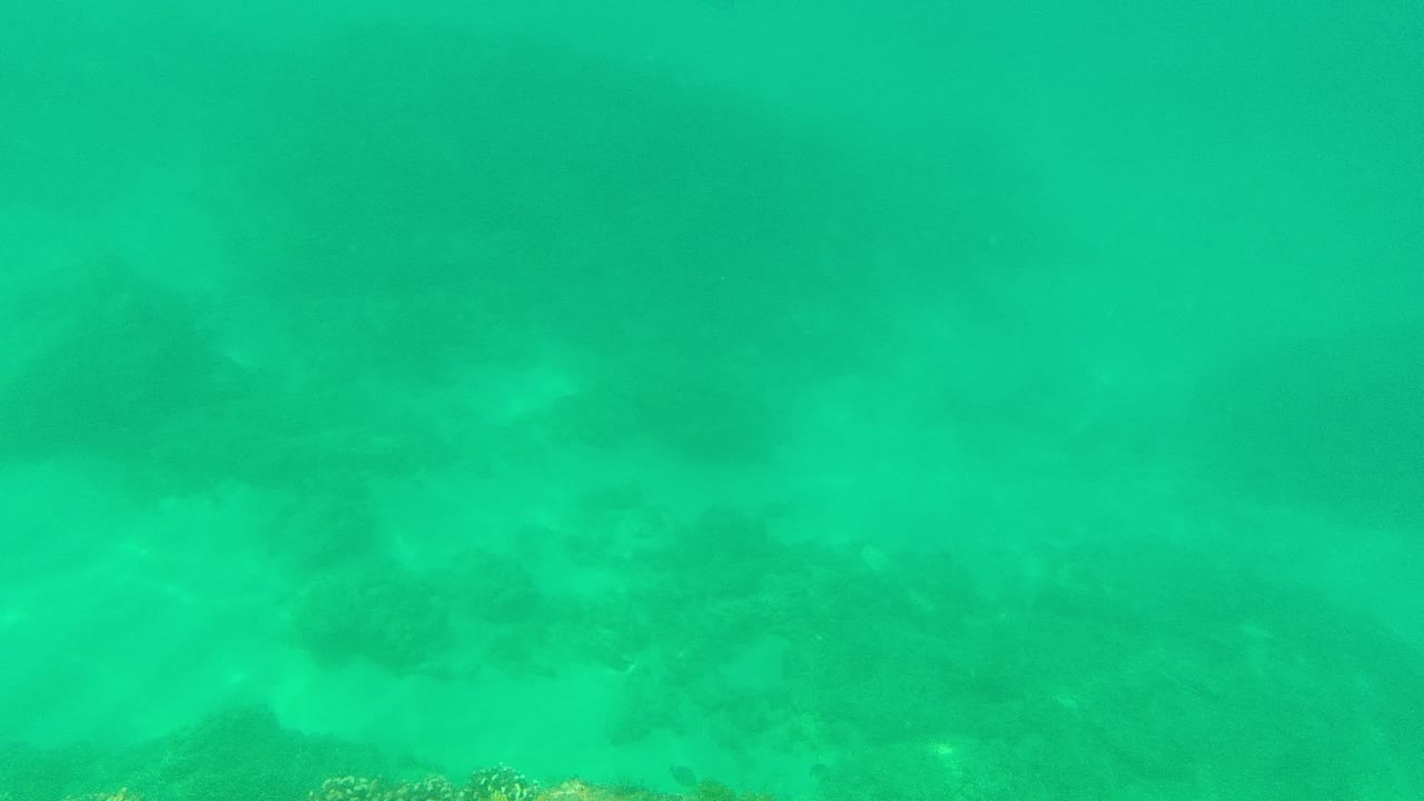 Turquoise underwater view of sandy seabed and scattered rocks.