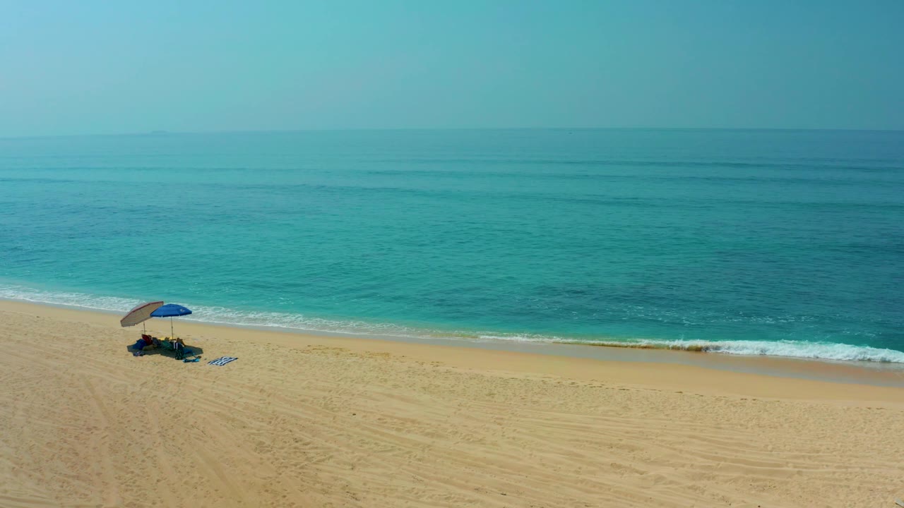 At Shipwrecks Los Cabos, the blue umbrella sits slightly left of center on the broad sand as a thin white wave line reaches the shore, with no visible people.