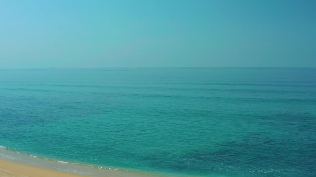 Wide aerial view at Shipwrecks Los Cabos with turquoise ocean, a thin sandy beach edge, clear sky, and no visible people.