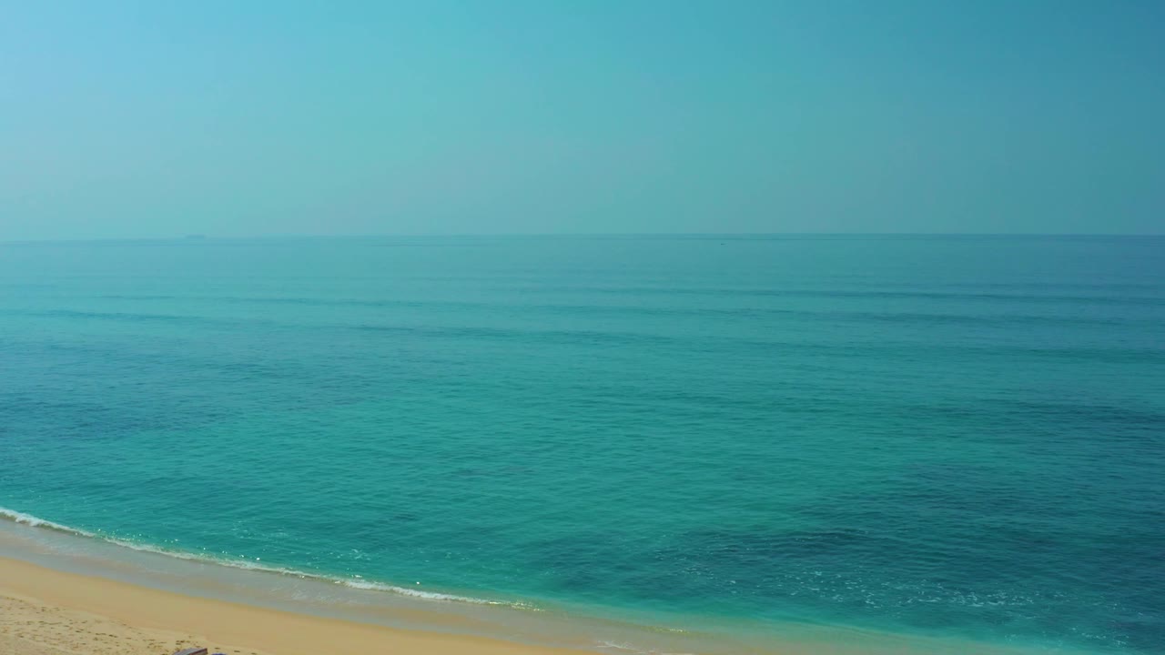 Aerial view at Shipwrecks Los Cabos with turquoise sea, sandy shoreline, a small glimpse of beach setup near the bottom edge, and no visible people.