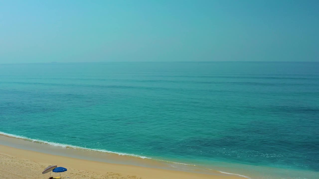 Sandy beach with turquoise ocean and blue umbrella near the lower left.