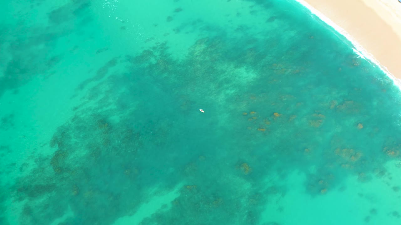 Overhead view at Shipwrecks Los Cabos where the beach edge shifts toward the upper right corner and darker underwater patches fill the middle of the turquoise water.