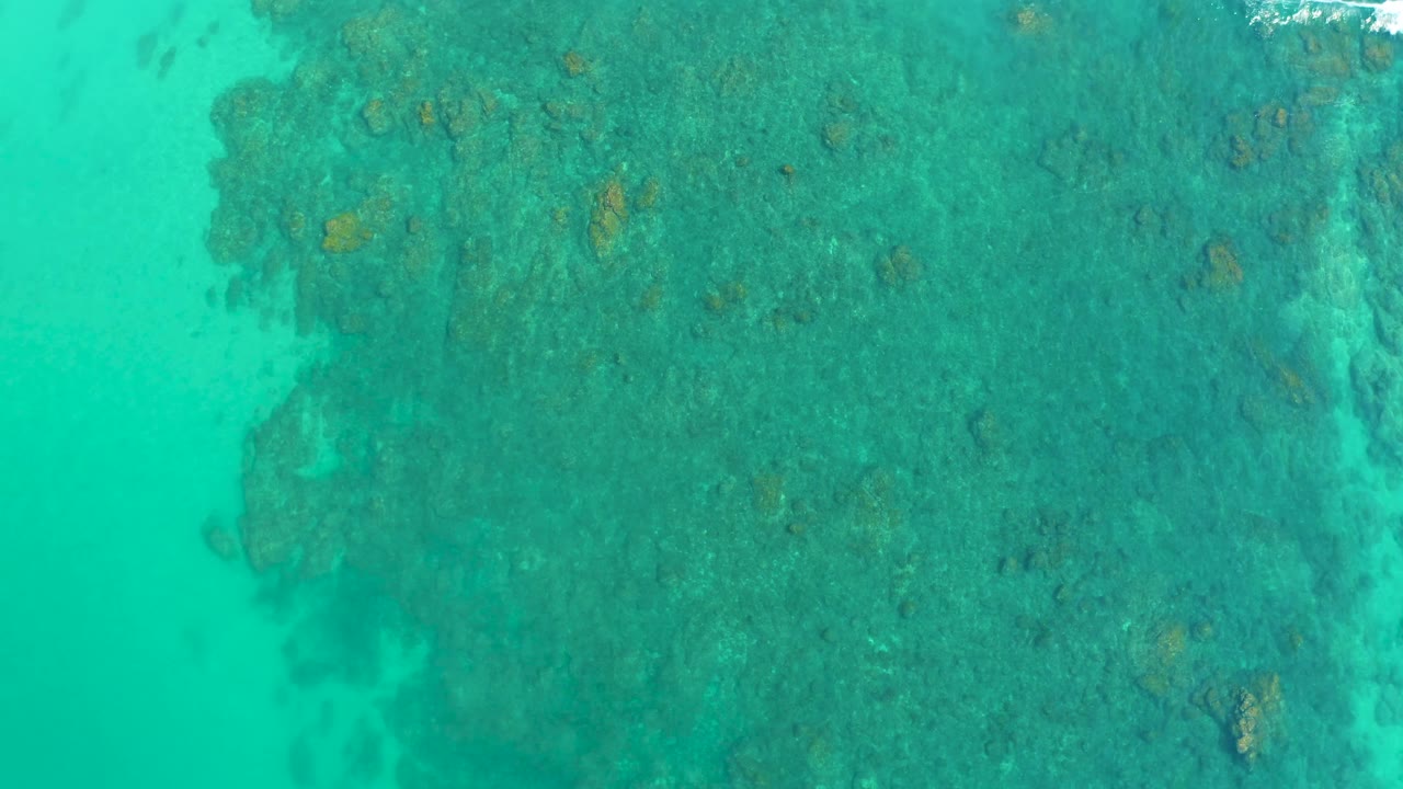 The overhead view at Shipwrecks Los Cabos shows open turquoise water on the left and a large darker reef area across the center and right, with no visible people.