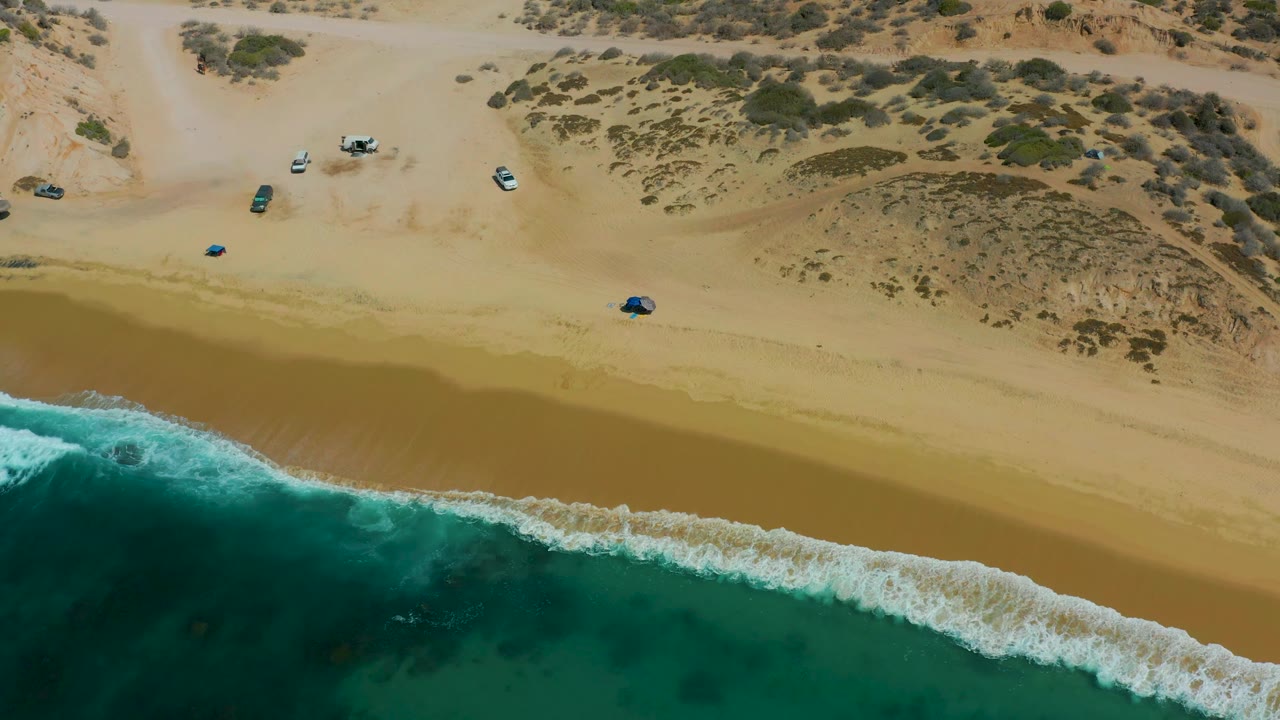 Diagonal wave line below sandy beach and parked vehicles