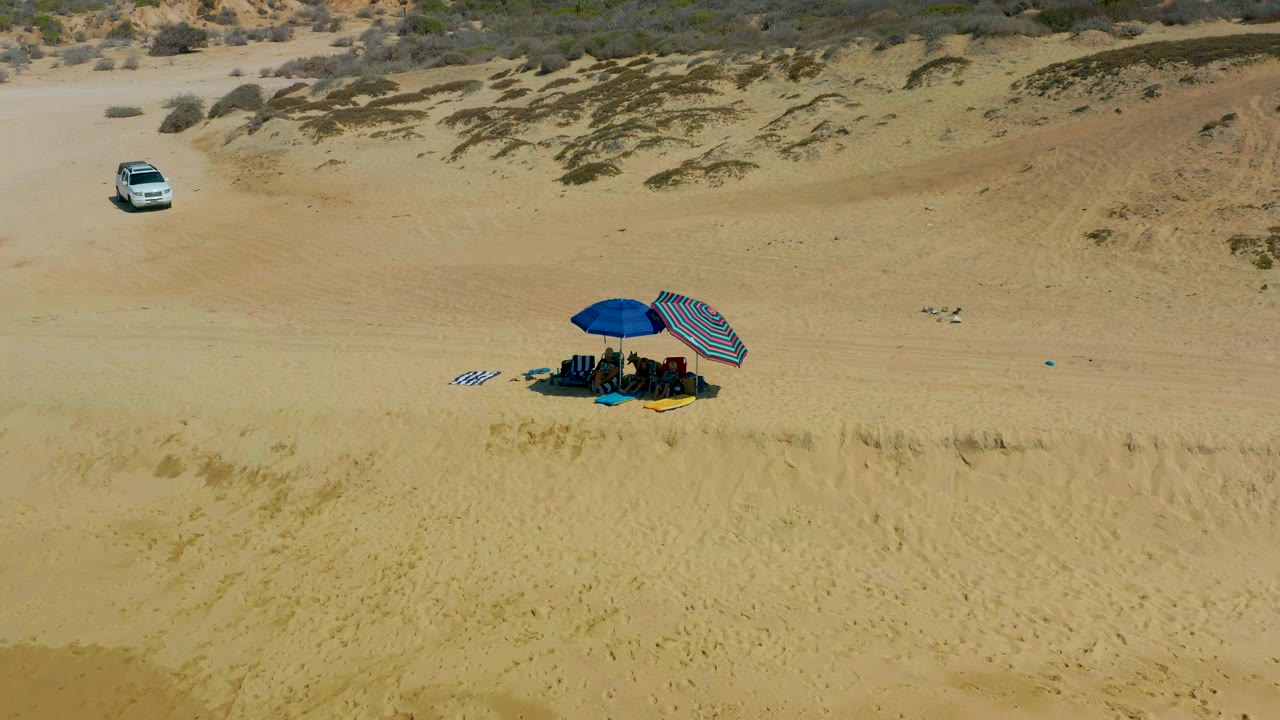 Beach camp with umbrellas below a white SUV on sand