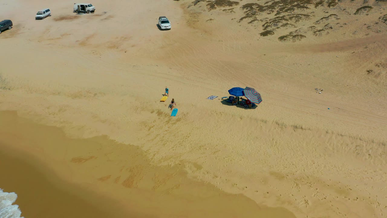 Overhead beach view with beachgoers near boards and parked cars above the sand